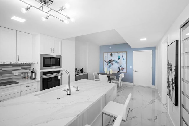 kitchen with a breakfast bar area, light stone countertops, white cabinets, and appliances with stainless steel finishes