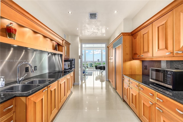 kitchen with brown cabinetry, visible vents, dark stone countertops, and a sink