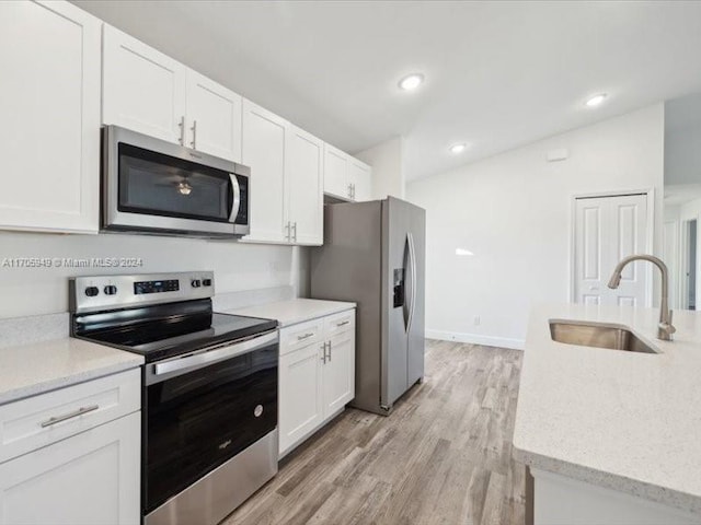 kitchen with sink, light stone countertops, appliances with stainless steel finishes, light hardwood / wood-style floors, and white cabinetry