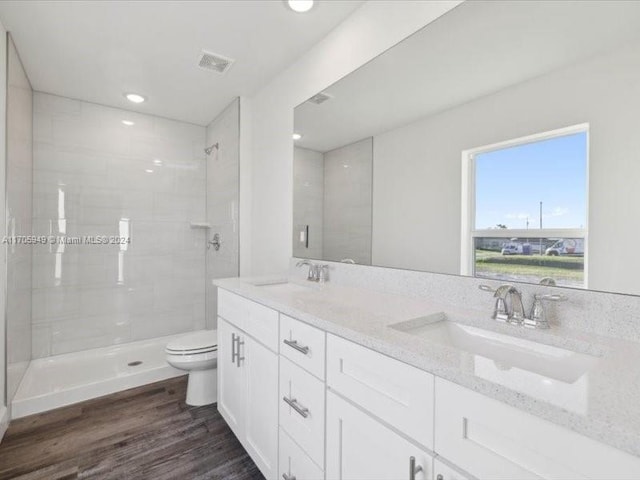 bathroom featuring a tile shower, vanity, wood-type flooring, and toilet