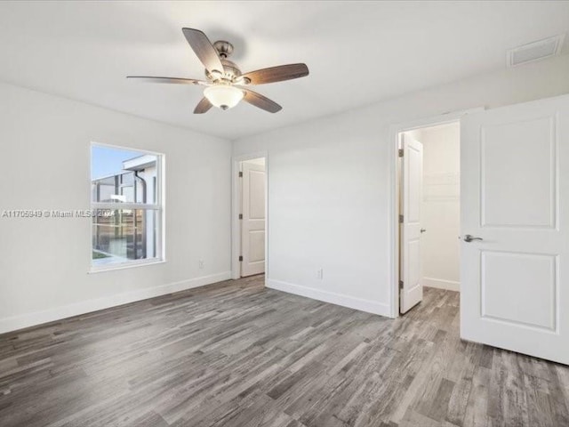 unfurnished bedroom with a closet, a spacious closet, ceiling fan, and light hardwood / wood-style flooring