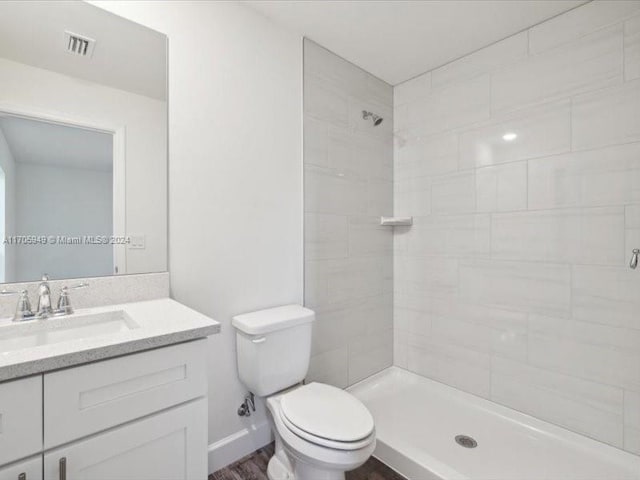 bathroom featuring tiled shower, vanity, hardwood / wood-style flooring, and toilet