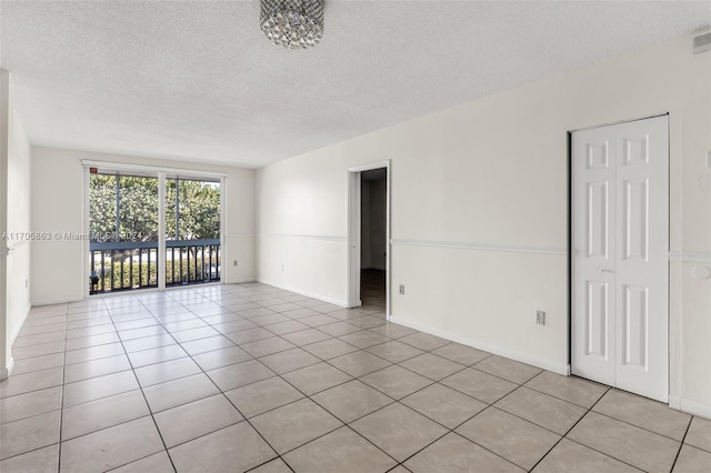 spare room with a chandelier, a textured ceiling, and light tile patterned flooring