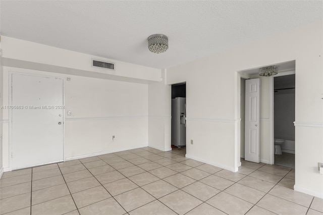 unfurnished bedroom with ensuite bath, stainless steel fridge with ice dispenser, light tile patterned floors, and a textured ceiling