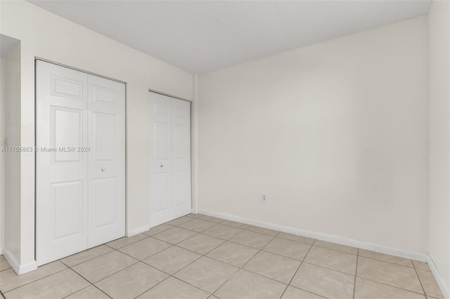 unfurnished bedroom with light tile patterned floors, a textured ceiling, and two closets