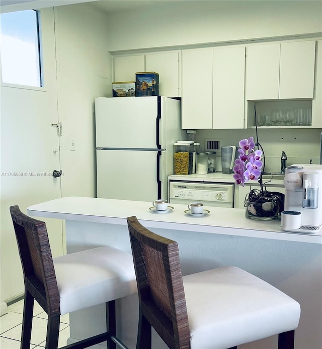 kitchen featuring white appliances, white cabinets, a kitchen breakfast bar, light tile patterned floors, and kitchen peninsula