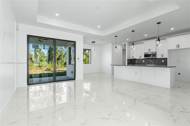 kitchen featuring decorative light fixtures, backsplash, a tray ceiling, and white cabinetry