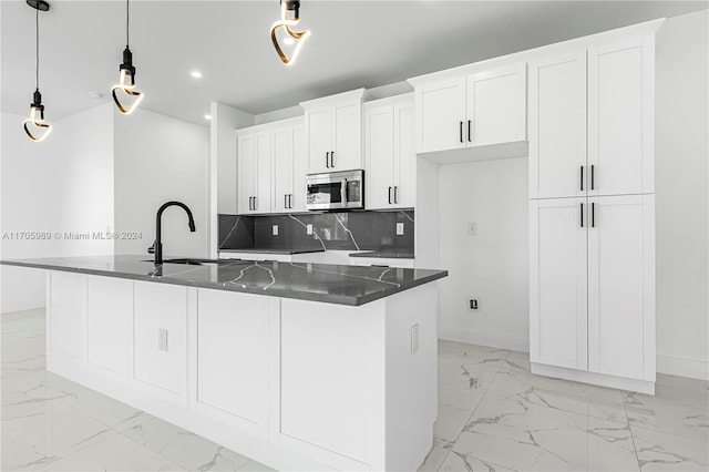 kitchen with a center island with sink, decorative light fixtures, white cabinets, and backsplash