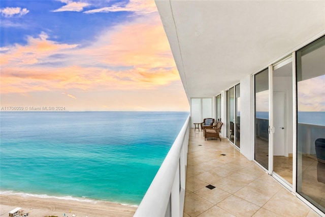 balcony at dusk with a water view and a view of the beach