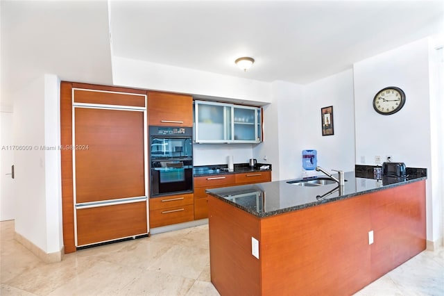 kitchen featuring dark stone counters, sink, paneled refrigerator, double oven, and kitchen peninsula