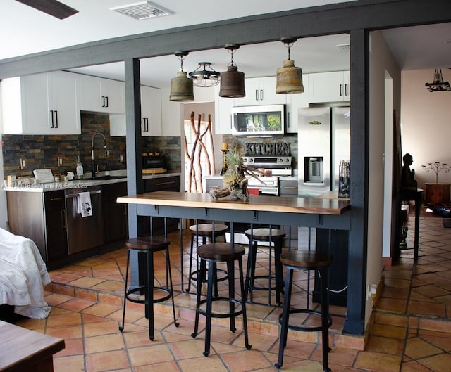 kitchen featuring appliances with stainless steel finishes, tasteful backsplash, white cabinets, hanging light fixtures, and dark brown cabinetry