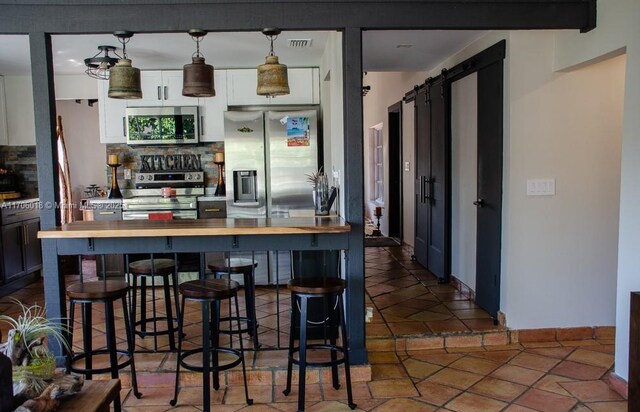 kitchen with appliances with stainless steel finishes, backsplash, wood counters, decorative light fixtures, and a barn door