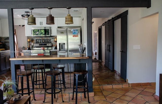 kitchen featuring butcher block countertops, tasteful backsplash, pendant lighting, stainless steel appliances, and a barn door