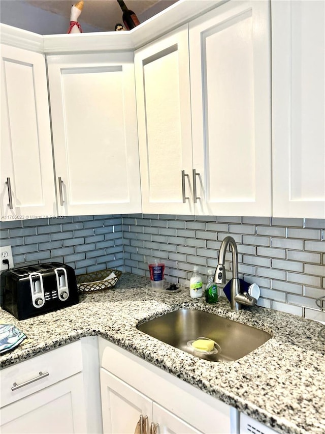 kitchen featuring tasteful backsplash, light stone countertops, sink, and white cabinets