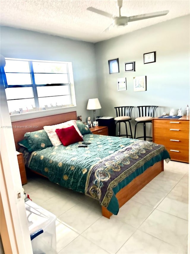 bedroom with ceiling fan, light tile patterned floors, and a textured ceiling