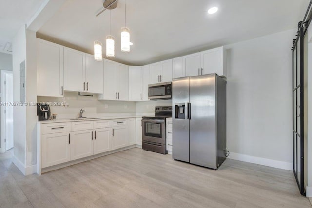 kitchen featuring appliances with stainless steel finishes, sink, decorative light fixtures, light hardwood / wood-style flooring, and white cabinets