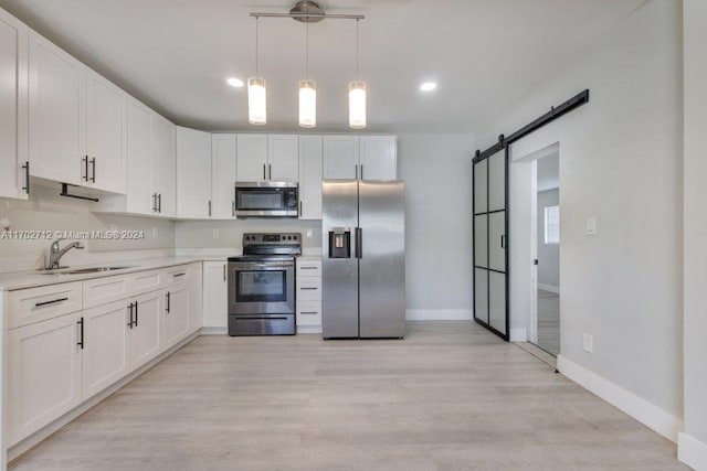 kitchen featuring white cabinetry, sink, stainless steel appliances, a barn door, and light hardwood / wood-style floors