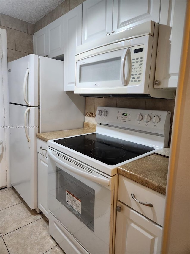 kitchen with a textured ceiling, white cabinetry, light tile patterned floors, and white appliances