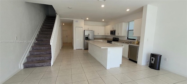 kitchen with stainless steel appliances, sink, white cabinetry, a kitchen island, and light tile patterned flooring