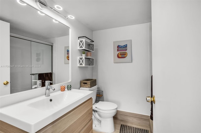 bathroom with hardwood / wood-style floors, vanity, toilet, and a shower with shower door