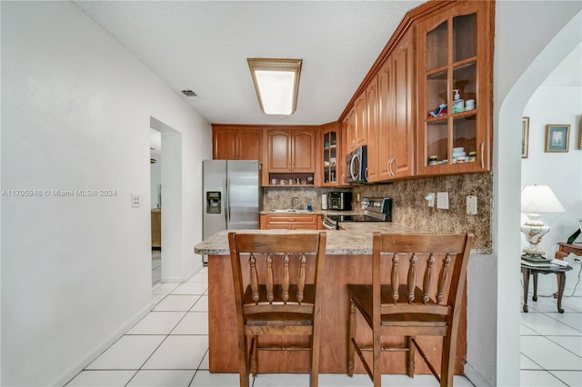 kitchen with kitchen peninsula, appliances with stainless steel finishes, backsplash, a breakfast bar, and light tile patterned floors