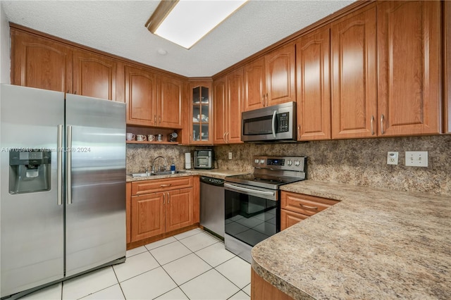 kitchen with appliances with stainless steel finishes, backsplash, a textured ceiling, sink, and light tile patterned flooring