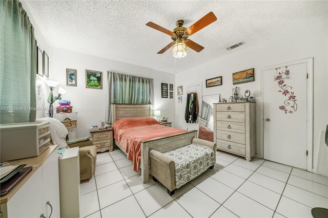 bedroom featuring ceiling fan, light tile patterned floors, and a textured ceiling