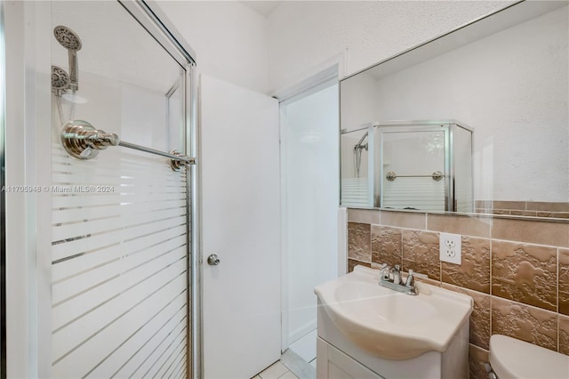 bathroom with vanity, a shower with door, tile patterned flooring, toilet, and tile walls