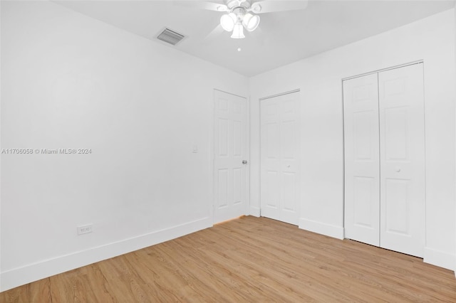 unfurnished bedroom featuring ceiling fan, light hardwood / wood-style flooring, and two closets