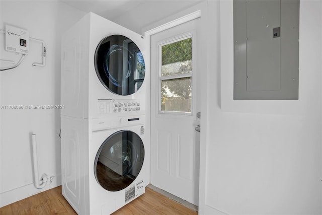 clothes washing area with wood-type flooring, electric panel, and stacked washer / drying machine