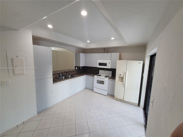 kitchen with white appliances, dark countertops, a tray ceiling, white cabinetry, and recessed lighting