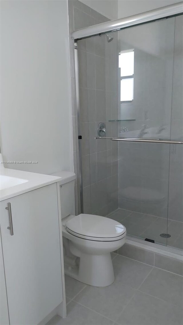 bathroom featuring toilet, vanity, tile patterned floors, and a shower with door