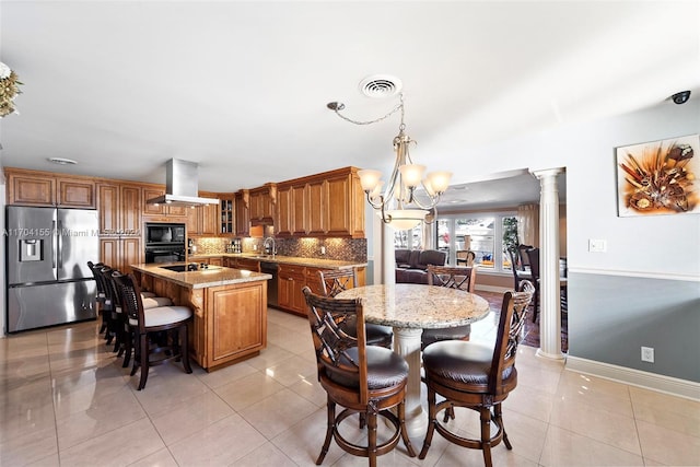 kitchen with a kitchen island with sink, black appliances, hanging light fixtures, ornate columns, and island range hood