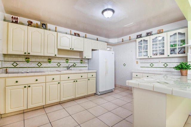 kitchen featuring tile countertops, light tile patterned floors, white fridge, and black electric cooktop