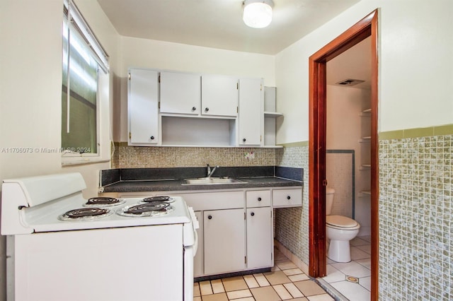 kitchen with electric stove, sink, tile walls, light tile patterned flooring, and white cabinetry