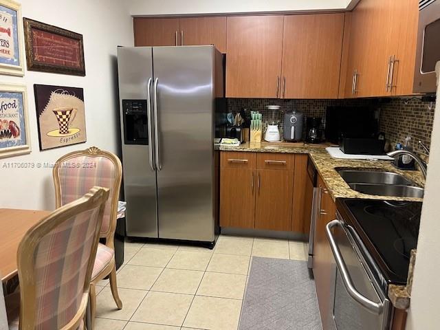 kitchen featuring decorative backsplash, light stone countertops, stainless steel appliances, sink, and light tile patterned floors