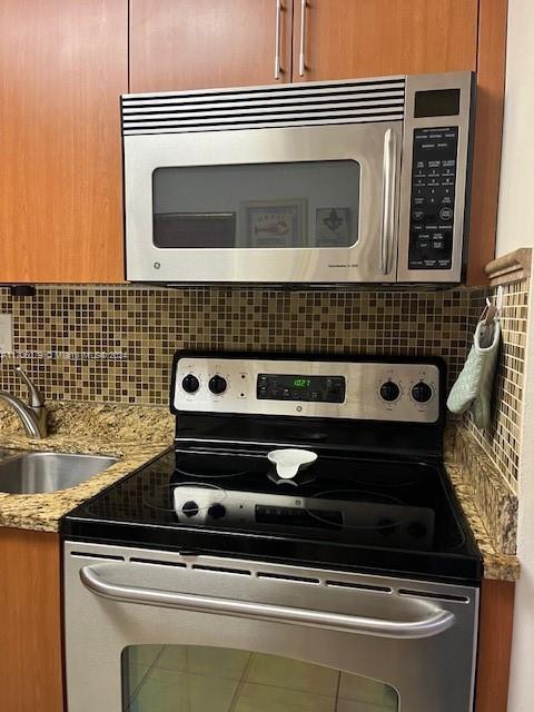 kitchen with decorative backsplash, stainless steel appliances, light stone countertops, and sink