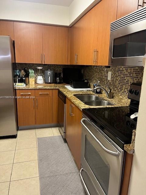 kitchen with sink, light tile patterned floors, light stone countertops, appliances with stainless steel finishes, and tasteful backsplash