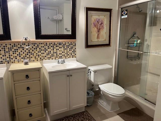 bathroom with vanity, tasteful backsplash, toilet, and a shower with door