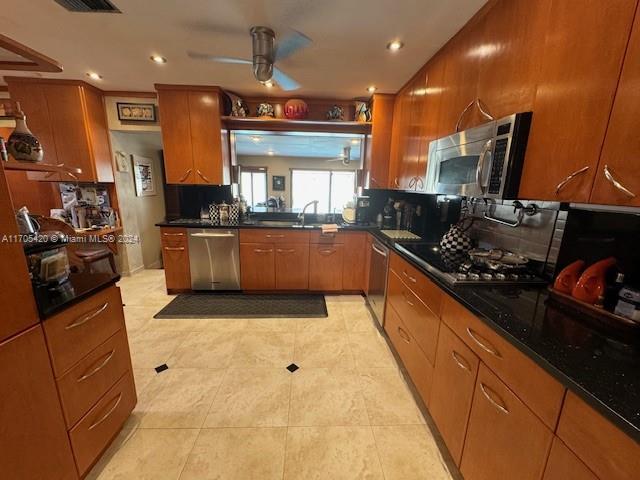 kitchen featuring ceiling fan, sink, stainless steel appliances, dark stone counters, and light tile patterned flooring