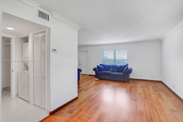 living room with ornamental molding, stacked washing maching and dryer, and light hardwood / wood-style floors