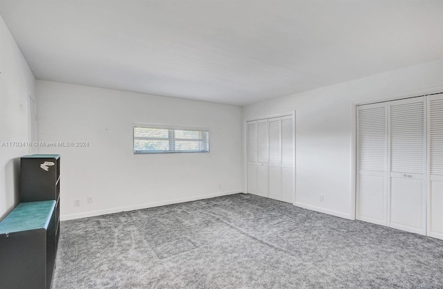 unfurnished bedroom featuring dark colored carpet and two closets