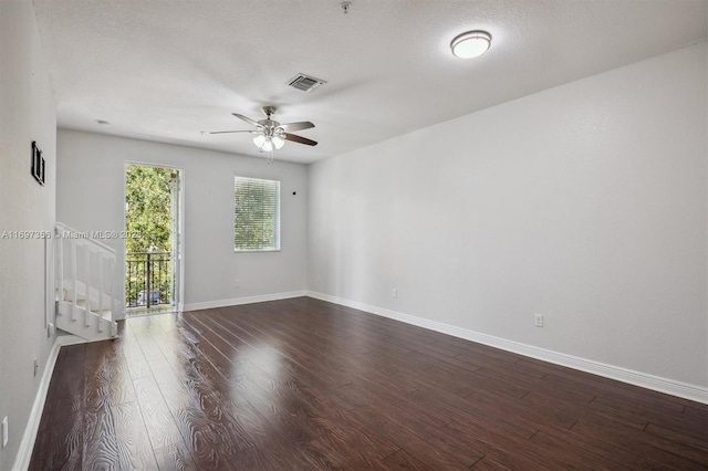 empty room featuring a textured ceiling, a ceiling fan, visible vents, baseboards, and dark wood finished floors