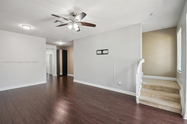 empty room featuring visible vents, baseboards, a ceiling fan, dark wood-style floors, and stairs