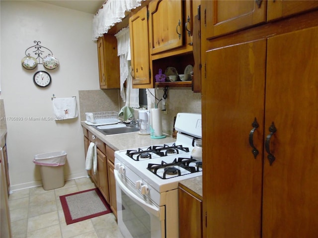 kitchen featuring white gas range, sink, and light tile patterned floors