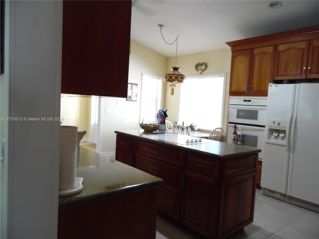 kitchen with pendant lighting, a kitchen island, light tile patterned flooring, and white appliances