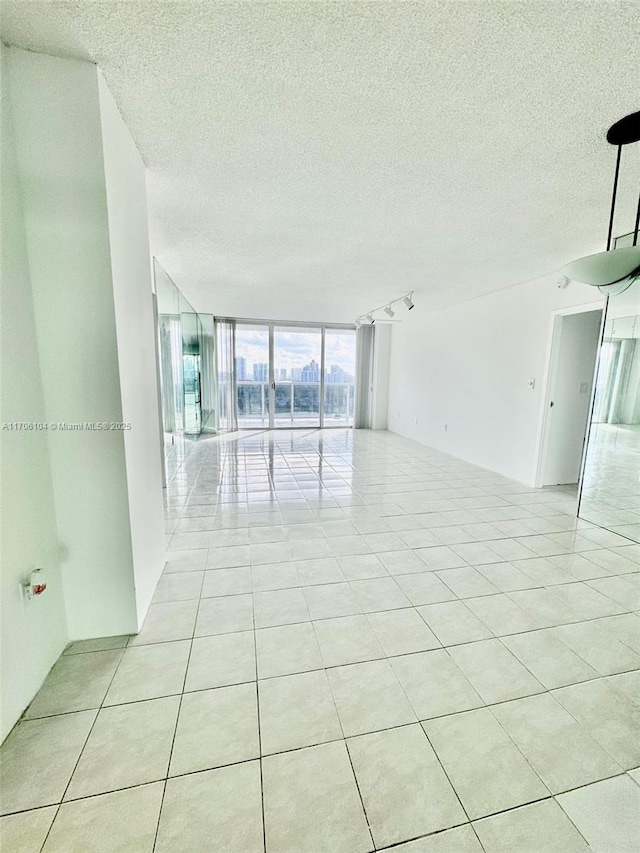 tiled empty room featuring track lighting and floor to ceiling windows