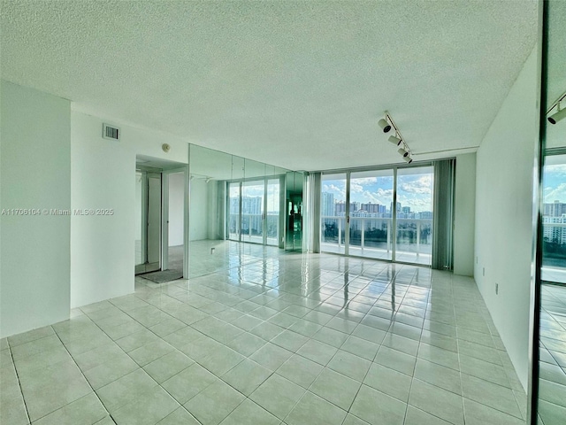 tiled empty room with track lighting, a healthy amount of sunlight, floor to ceiling windows, and a textured ceiling