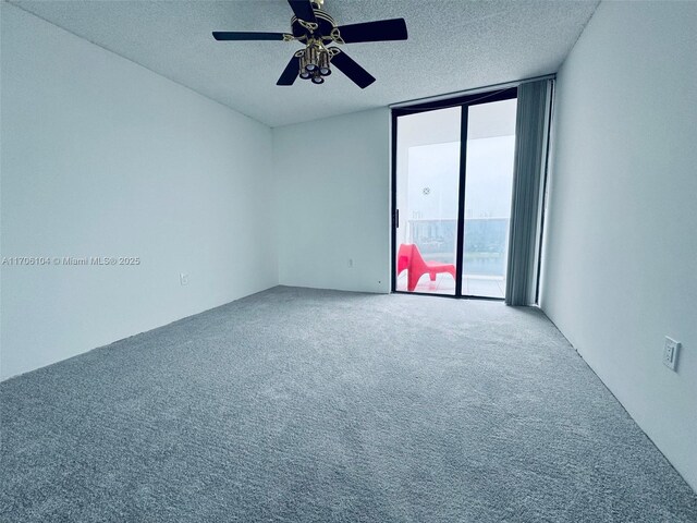 empty room with a textured ceiling, expansive windows, ceiling fan, and carpet