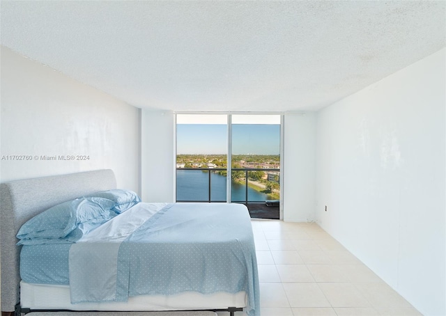 bedroom featuring floor to ceiling windows, access to exterior, a textured ceiling, and a water view